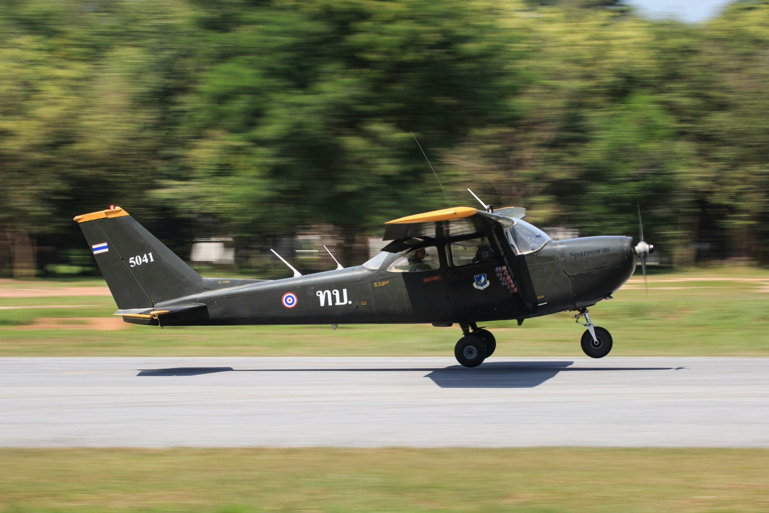 A military aircraft in motion as it lands on a runway surrounded by greenery.